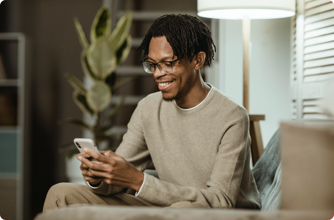 homem preto, vestido com moleton bege  sorrindo olhando para o celular